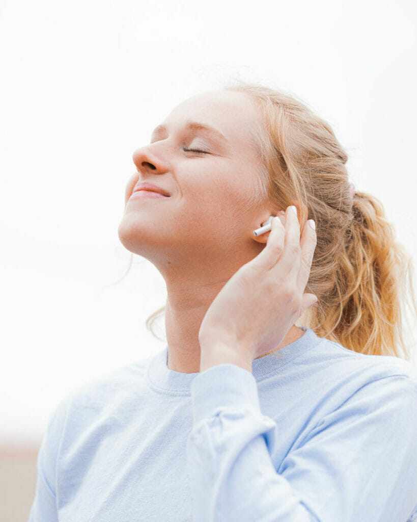 White woman with strawberry blonde hair listens to music with airpods