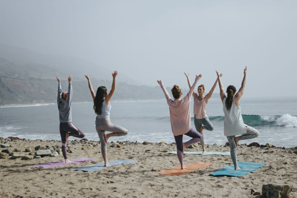 Positive Female Practising Yoga Poses At Seaside In Evening