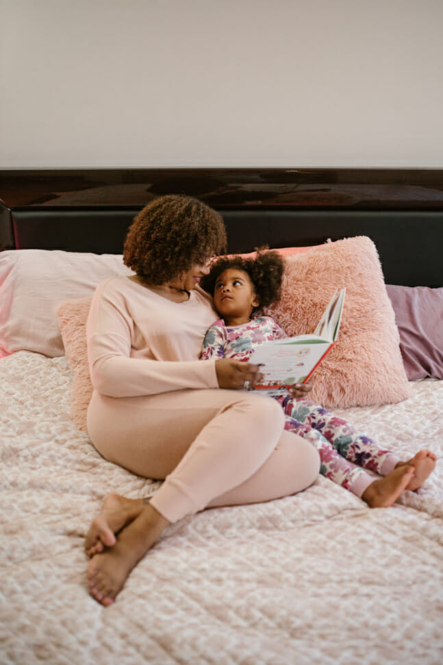 Black mother and her daughter read a story to put the toddler to sleep