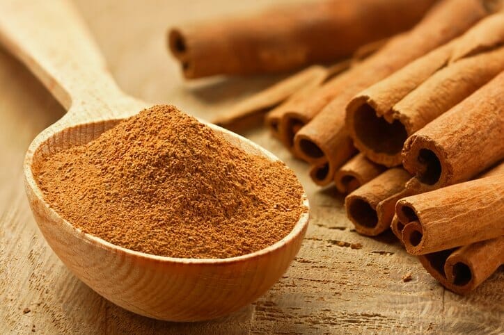 Image of ground cinnamon in a spoon next to cinnamon sticks which is a food for period pain