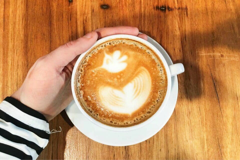 finding flow over your morning coffee - image of a cup of coffee on wood with a hand wrapped around the cup