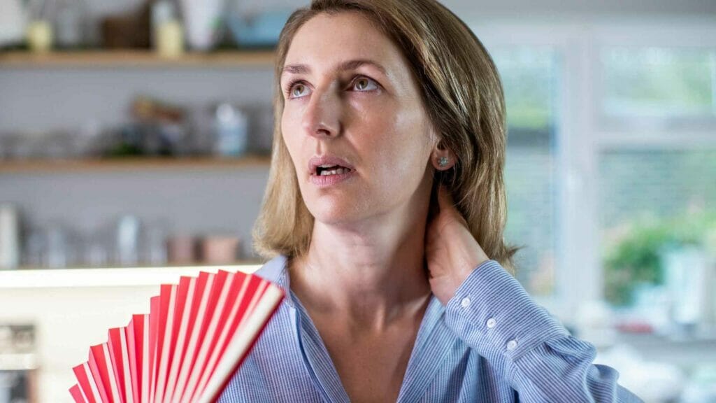 A woman cools herself with a fan due to perimenopause or menopause symptoms