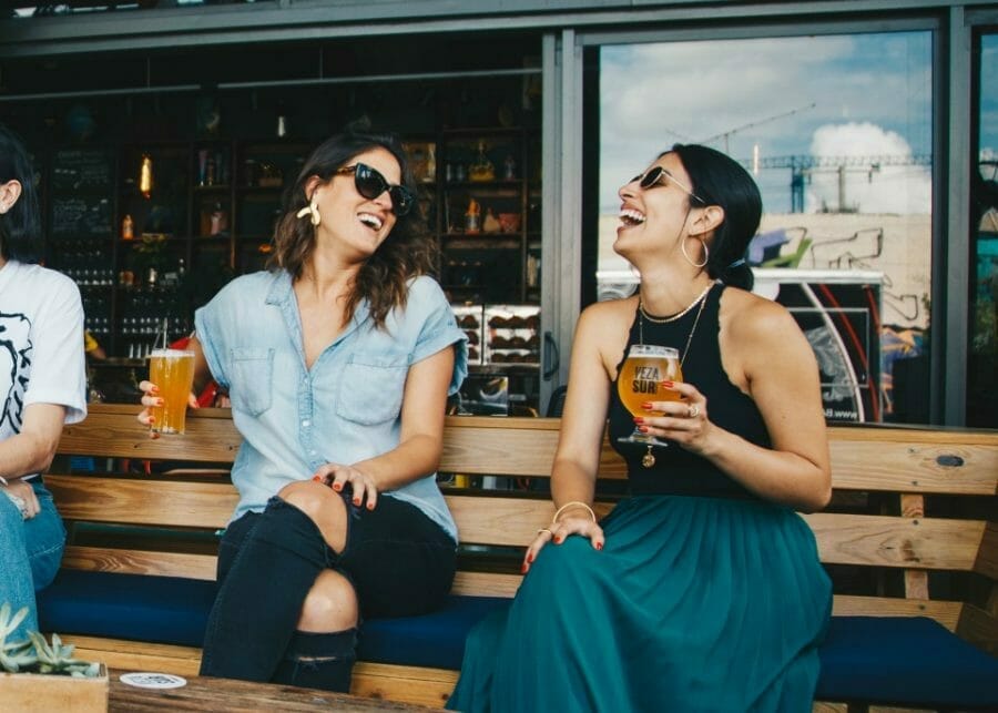 Two women enjoying a beer at a pub laughing - positive people help build self-esteem