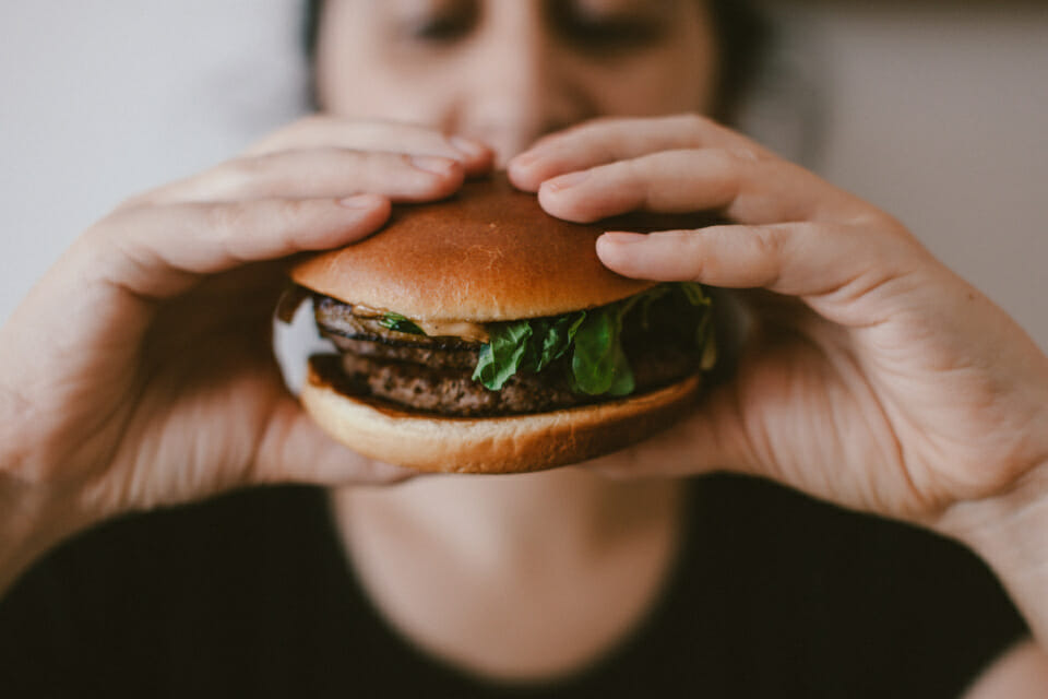 Person eating a hamburger which is definitely one of the foods that make you happy