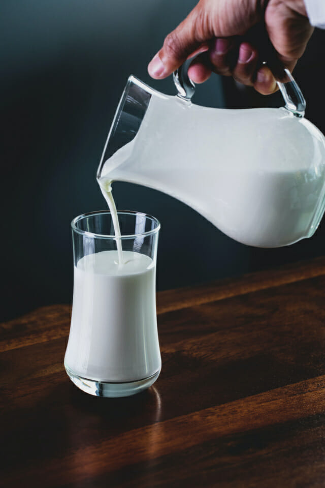 Image of a jug of milk being poured into a glass on a wood table, milk helping with menstrual cramps