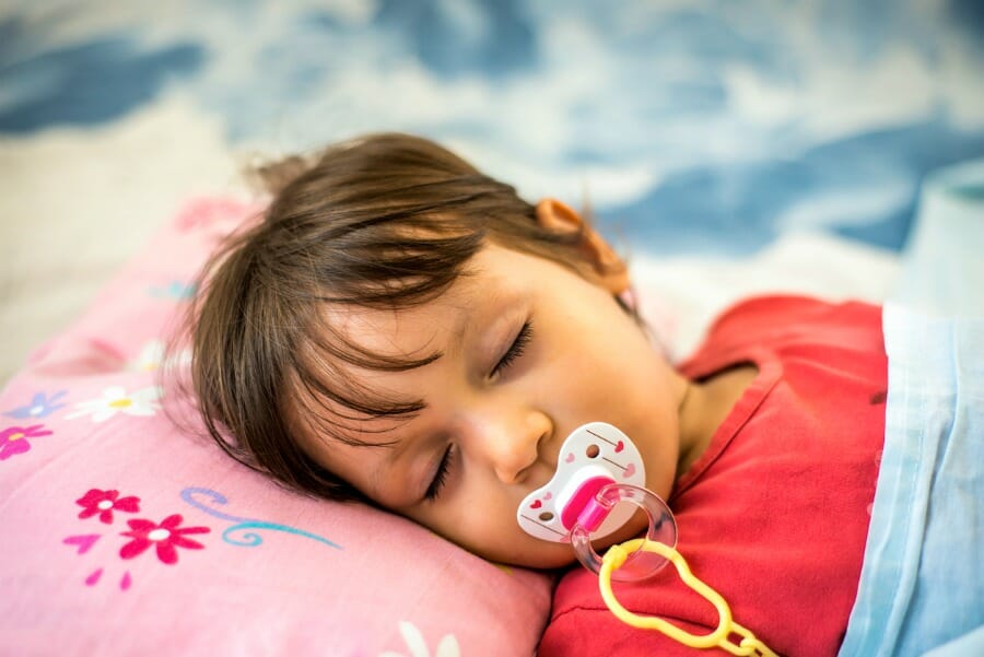 Image of a sleeping baby with dummy after the parents followed the tips to help your kids sleep better