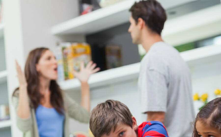 Couple fighting in the background with children looking stressed in the foreground indicating relationship stress has impact on children