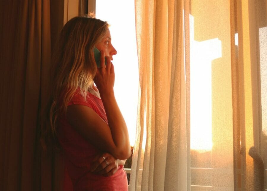 Woman on the phone by a window in a darkened room speaking to a counsellor for her mental health