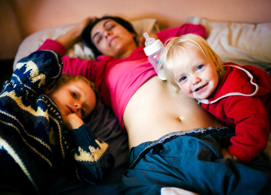 Image of an exhausted mum asleep with kids piled on top of her wondering how the mum can help your kids sleep better