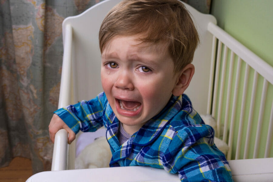 Image of a crying toddler standing up in their crib - help your kids sleep better