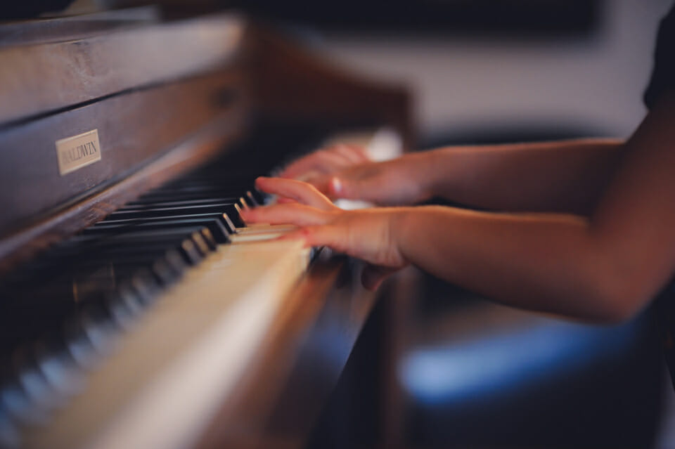 A black child's hands play an upright wooden piano showcasing his interest in music which they show their parents who have helped them improve your child's self-awareness