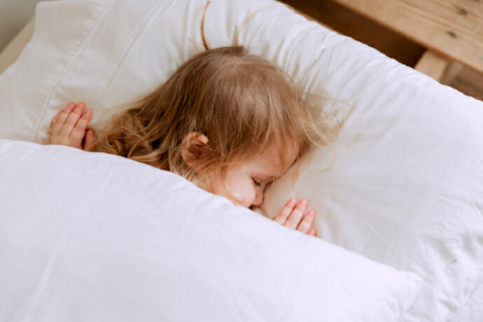 Image of child face down in bed asleep after their parents followed tips to help kids sleep at night