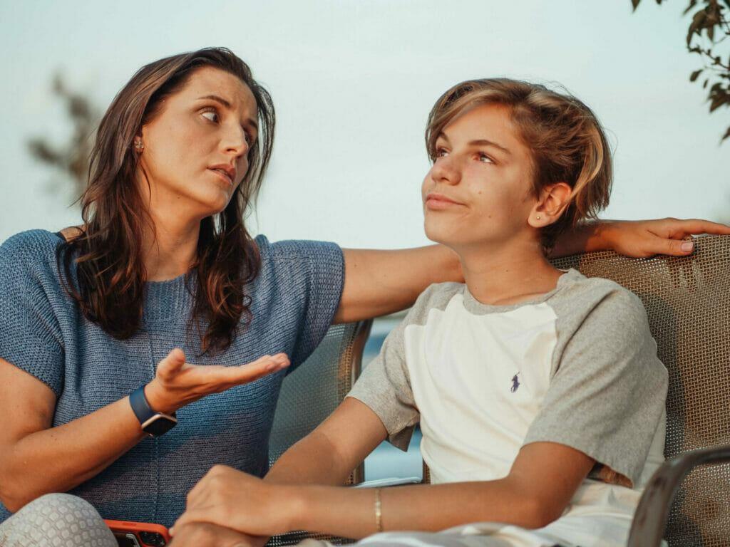 A frustrated-looking white mother is sitting talking to her son who looks distracted due to his childhood ADHD symptoms