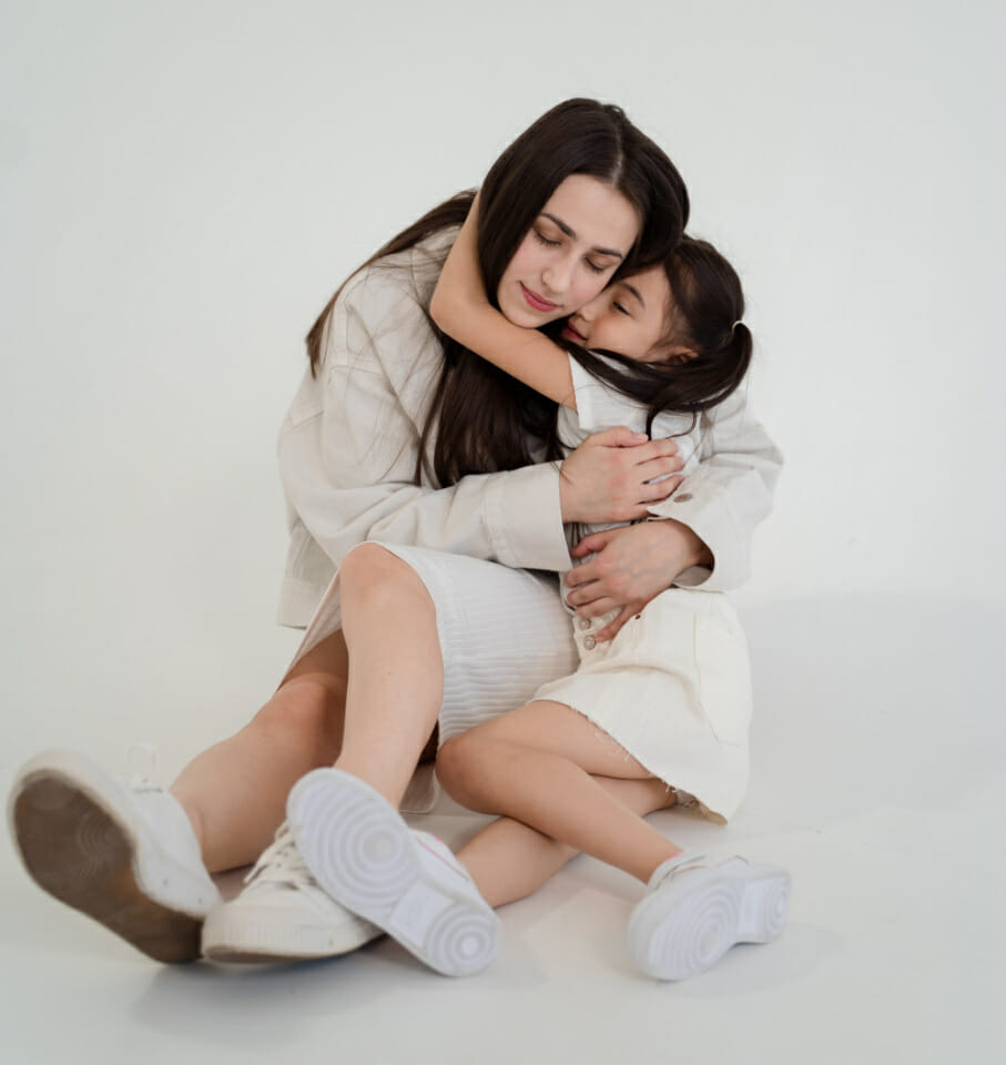 Mother and daughter embrace in a hug on white background showcasing how following your lead can help improve your child's self-awareness